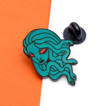 Teal Medusa enamel lapel pin with red eyes and black metal outlines against an orange and white background.