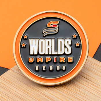 Circular challenge coin with Worlds Umpire Heads text, stars, and logo on black and orange enamel.