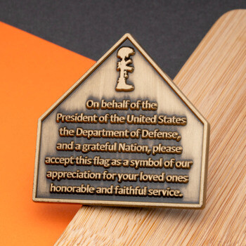 Antiqued bronze house-shaped challenge coin featuring a military tribute message from the Department of Defense and a folded flag icon.