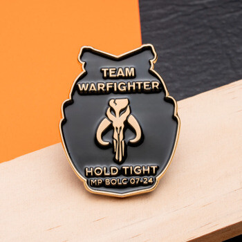 Black and gold Team Warfighter lapel pin featuring a mythosaur skull emblem and the text Hold Tight MP BOLC 07-24.