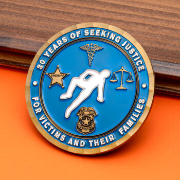 Blue and gold challenge coin featuring a chalk outline, sheriff star, caduceus, and scales of justice symbols.