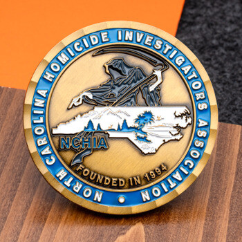 Gold challenge coin for the North Carolina Homicide Investigators Association featuring a grim reaper, the NC state silhouette, and blue enamel border.