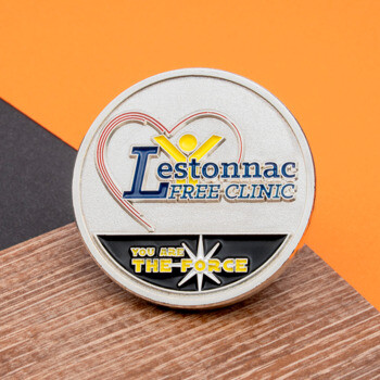 Lestonnac Free Clinic challenge coin with heart logo and You Are The Force text on a silver and black background.