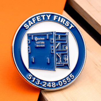 Round challenge coin with blue enamel featuring trench safety equipment and Safety First text.